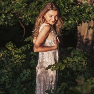 Femeie în rochie lungă, cu mâinile pe piept, în grădină: programul online Breast Care Love